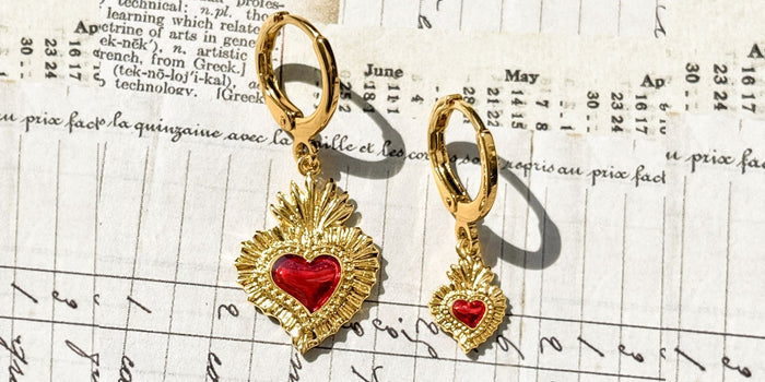 Fortune & Frame Sacred Heart gold mismatched earrings on a paper background with script handwriting.